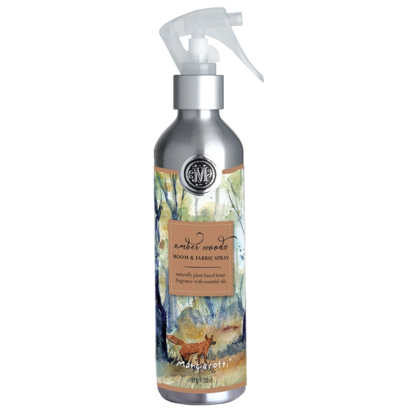 A spray bottle labeled "NEW! Amber Woods Room & Fabric Spray" by Mangiacotti, featuring an elegant design with a watercolor forest scene and a deer.