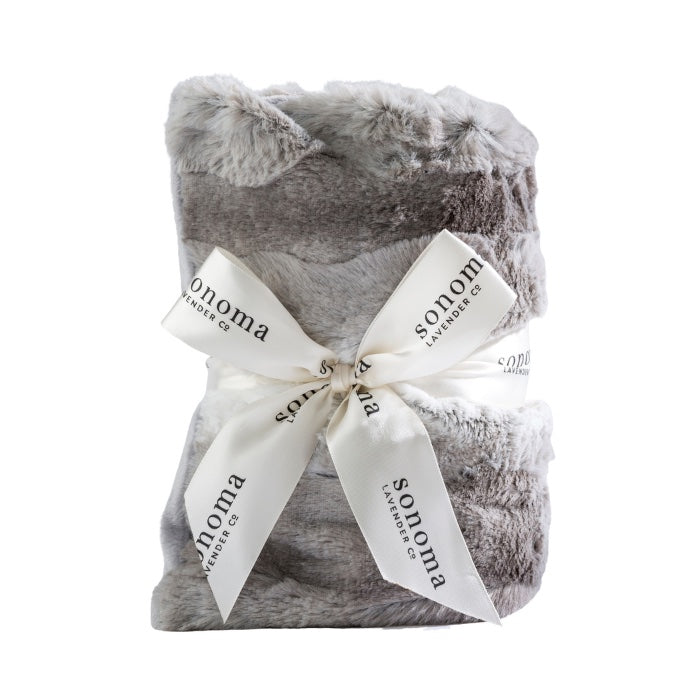 A folded Sonoma Lavender Angora Platinum Heat Wrap tied with a ribbon printed with the word "sonoma" against a white background, infused with lavender flowers.