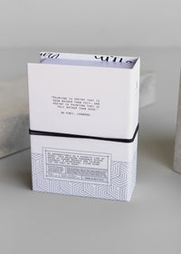 A stack of white notebooks with one open on top revealing a quote from Leonardo da Vinci about painting and poetry. The cover shows an intricate geometric design of Archive by Margot Elena - Poet at Heart Fragrance.