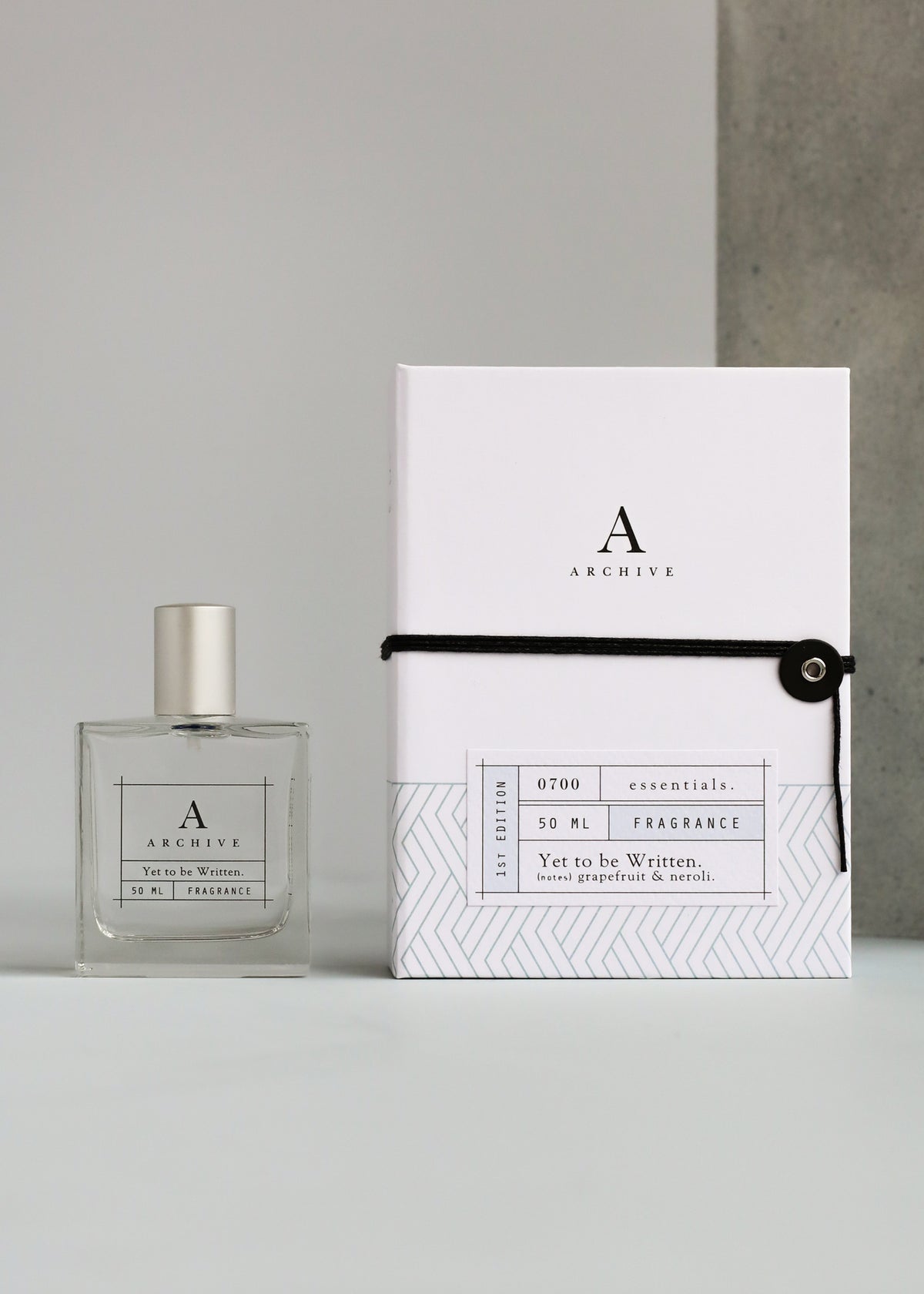 A bottle of ARCHIVE by Margot Elena - Yet to be Written Fragrance perfume next to its keepsake box, displayed against a plain gray background. The box is white with black text and a geometric design.