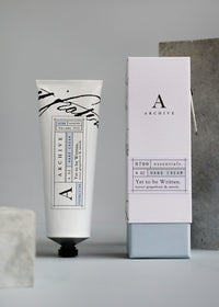 A tube of "ARCHIVE by Margot Elena - Yet to be Written Hand Cream" beside its packaging box, set against a neutral backdrop. The tube and box feature stylish, modern labels in black and white with a minimalist design, infused with revitalizing citrus notes.