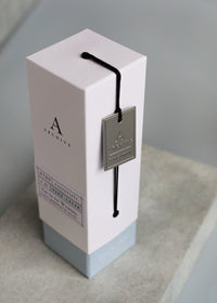 A sleek, light gray Archive by Margot Elena product box for "Yet to be Written Hand Cream", featuring elegant text and minimalist design, with a silver metallic tag scented with revitalizing citrus hanging by a black string.