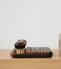 A French Andrée Jardin Heritage Ash Soap Holder with a natural pattern and an accompanying Andrée Jardin brush with dense bristles, sitting on a smooth wooden surface against a plain light background.