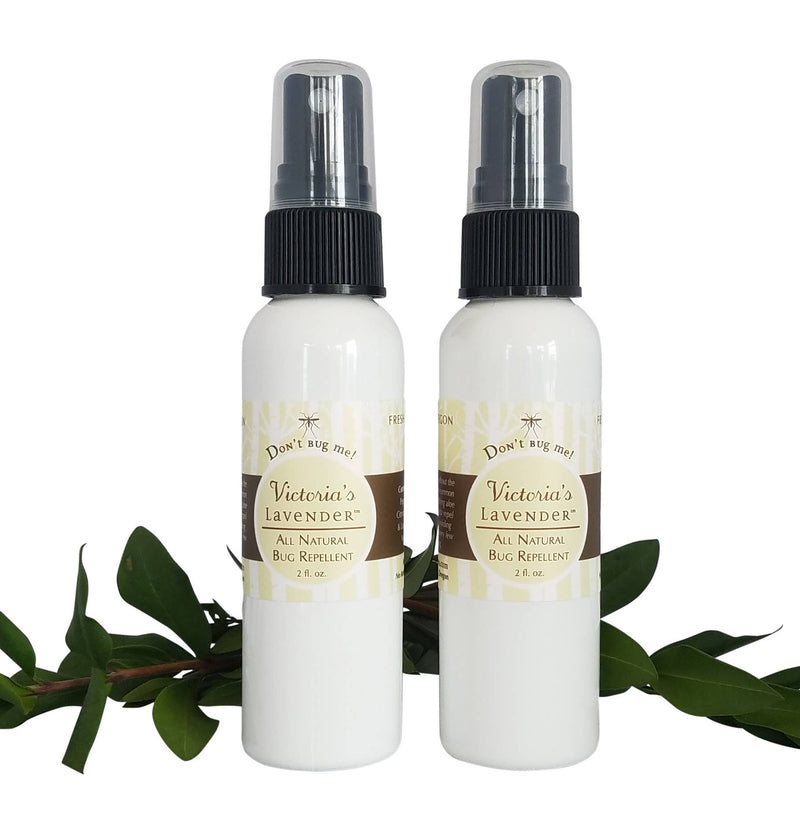 Two bottles of Victoria's Lavender "Don't Bug Me!" All Natural Bug Spray - 2oz, each labeled with lavender graphics, placed on a white background with green leaves accenting the lower part of the image