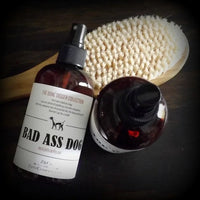 Amber-colored glass bottles of Z&Co. grooming products with natural ingredients and a wood-handled brush on a dark surface, labeled for a "bad ass dog" from the Z&Co. Bone Digger Collection.