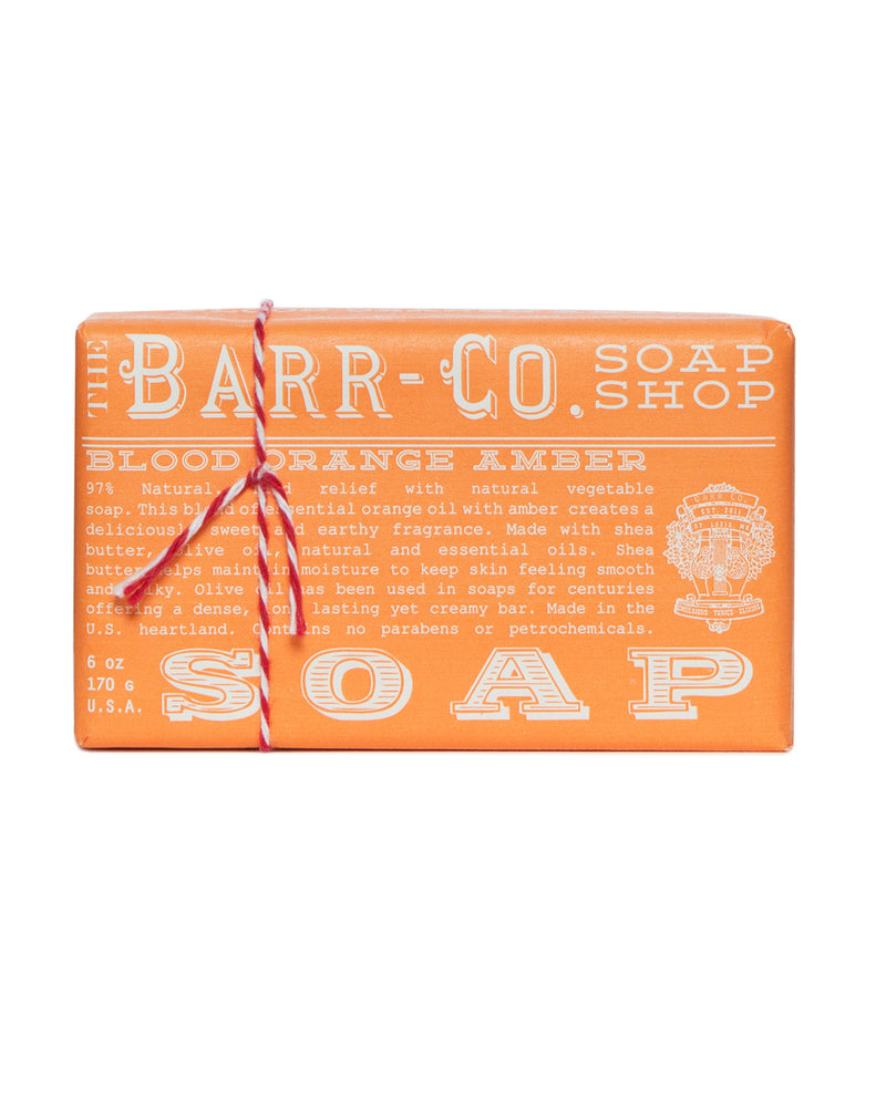 A bar of Barr-Co. Blood Orange Amber Triple Milled Bar Soap, wrapped in orange paper tied with a red and white striped string, with detailed product information and ingredients listed on the packaging.