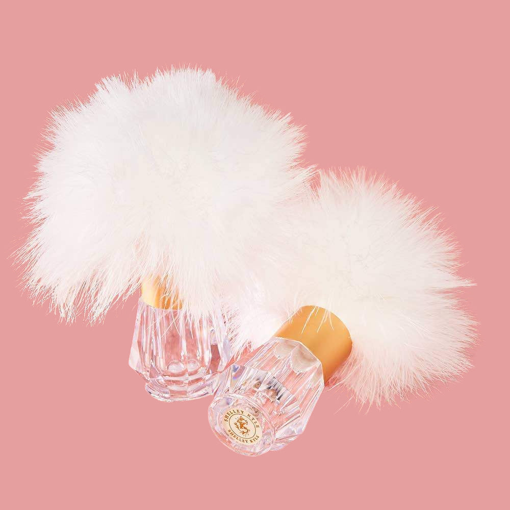 Two elegant, cruelty-free Crystal Body Duster bottles with fluffy white atomizer pumps on a soft pink background from Odds & Ends.