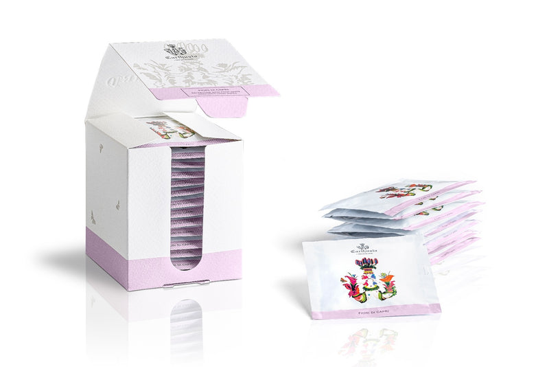 An open white Carthusia I Profumi de Capri Fiori di Capri Perfumed Hand Wipes box with a floral design, displaying numerous individual Carthusia hand wipes arranged neatly inside. Several hand wipes are also placed beside the box on a reflective surface.
