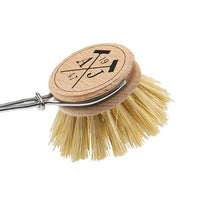 A round, wooden Andrée Jardin Tradition Handled Dish Brush with natural, compostable bristles and a metal handle, featuring laser-engraved runes or symbols on top of the wooden part. The image is set against a white background.