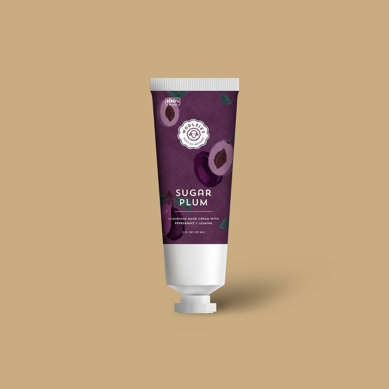 A tube of Woolzies Sugar Plum Holiday Hand Cream 2oz from Woolzies, featuring a purple floral design on the label and formulated with natural Sugar Plum ingredients, displayed against a beige background.