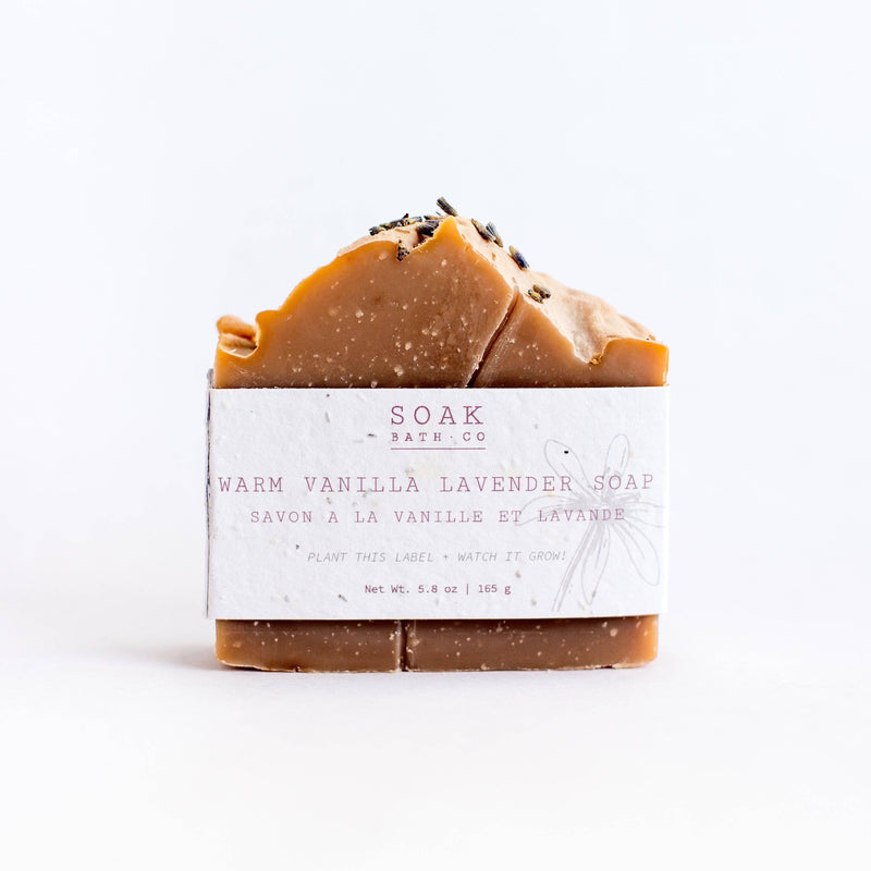 A bar of SOAK Bath Co. - Warm Vanilla Lavender Soap with a caramel drizzle on top, wrapped in a white label on a bright white background, promoting zero waste and sustainability.