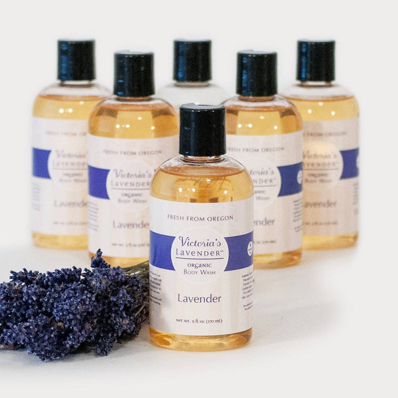A collection of six clear, sulfate-free bottles labeled "Victoria's Lavender - Lavender Organic Body Wash," with a bundle of fresh lavender in the foreground.