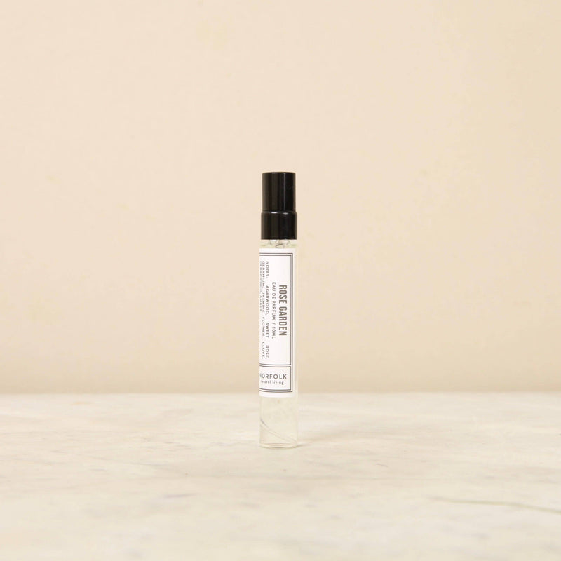 A Norfolk Natural Living Rose Garden Parfum 10ml with a white label and black text, featuring a long-lasting fragrance, standing on a light beige surface against a neutral background.