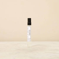 A small, cylindrical glass spray bottle with a black cap sits on a light-colored marble surface against a beige background. The bottle has a white label with black text that reads "Norfolk Natural Living Parfum - Rose Garden 10ml" and "Norfolk Natural Living," promising a long-lasting fragrance.