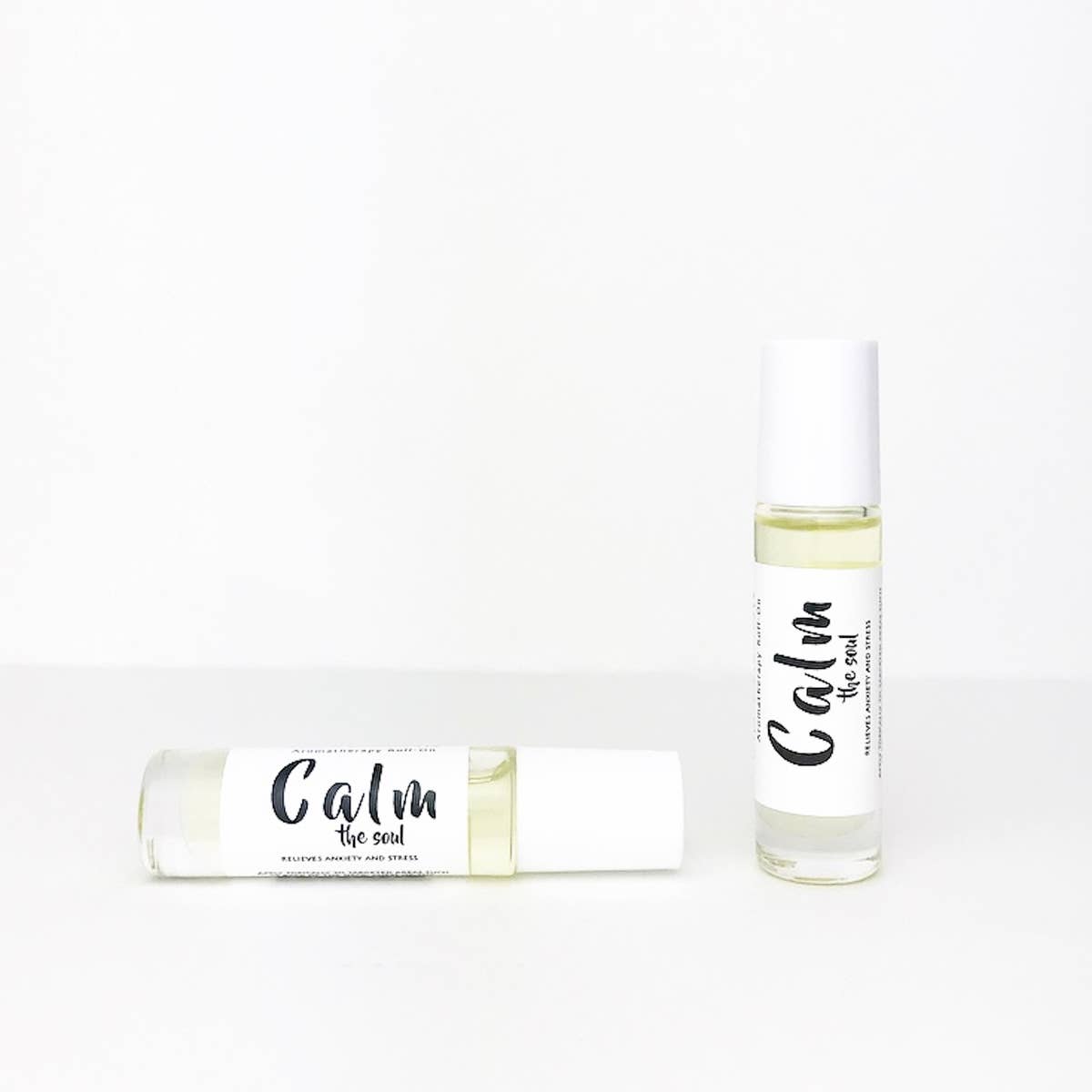 Two cylindrical bottles of Wild Botanicals Calm Aromatherapy Roll-On essential oils rest against a plain white background, one standing upright and the other lying horizontally, both featuring clean, simple labels.