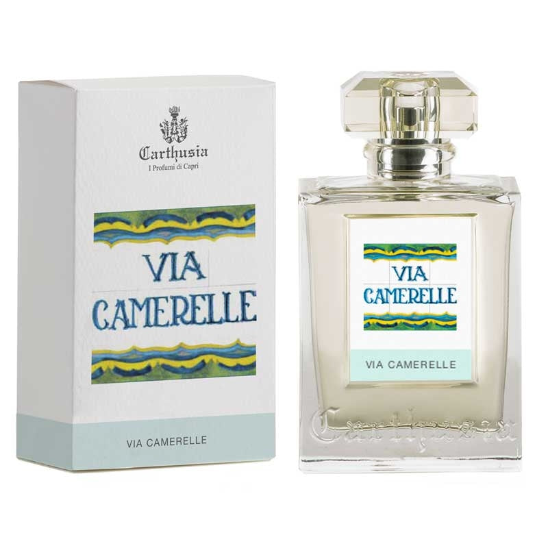 A picture of a Carthusia Via Camerelle Eau de Parfum bottle next to its packaging box. The bottle is clear with a square shape and a classy stopper on top. The box is white with blue and yellow wavy patterns. Brand Name: Carthusia I Profumi de Capri
