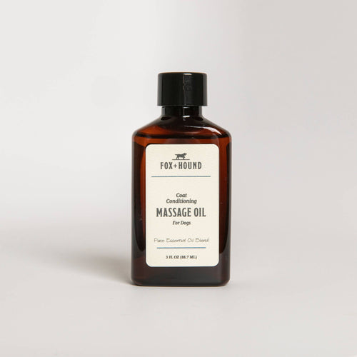 A brown glass bottle labeled "Fox + Hound Coat Conditioning Massage Oil" stands against a white background. The label includes further product details.