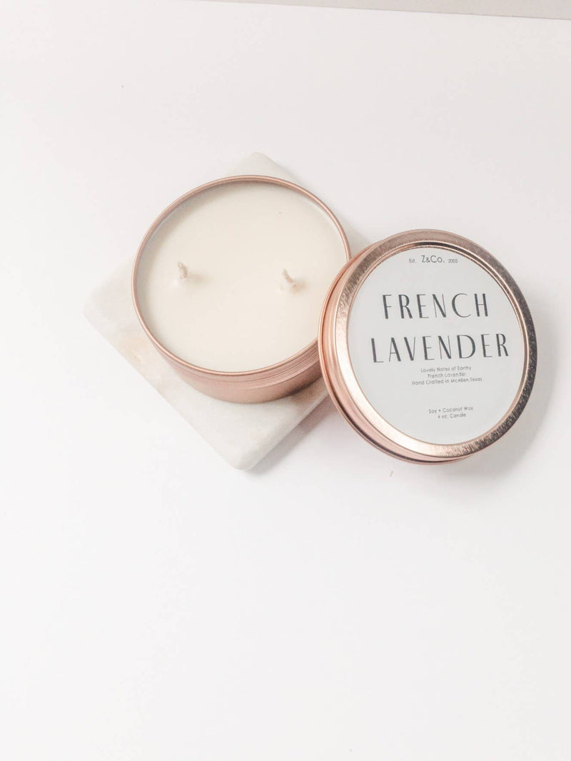 A Z&Co. French Lavender Rose Gold Candle made of soy coconut wax in a two-wick rose gold container with a decorative lid, resting on a white surface.