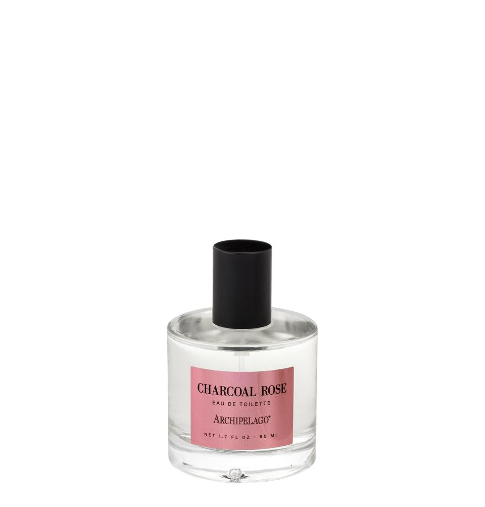 A clear glass perfume bottle labeled "Archipelago Charcoal Rose Eau de Toilette" by Archipelago Botanicals, containing a pink-tinged liquid, with a black cap, isolated on a white background.