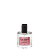 A clear glass perfume bottle labeled "Archipelago Charcoal Rose Eau de Toilette" by Archipelago Botanicals, containing a pink-tinged liquid, with a black cap, isolated on a white background.