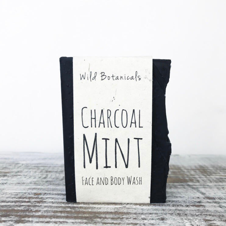 A bar of Wild Botanicals Charcoal Mint Soap, enhanced with shea butter, standing upright on a wooden surface with a simple, rustic background.