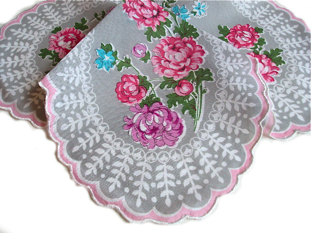 A Vintage-Inspired Hanky - Clover-Shaped Mum Hanky with an embroidered design of pink and blue flowers, featuring intricate lace edges with pink trim, displayed on a clover-shaped handkerchief background by Hankies ala Carte.
