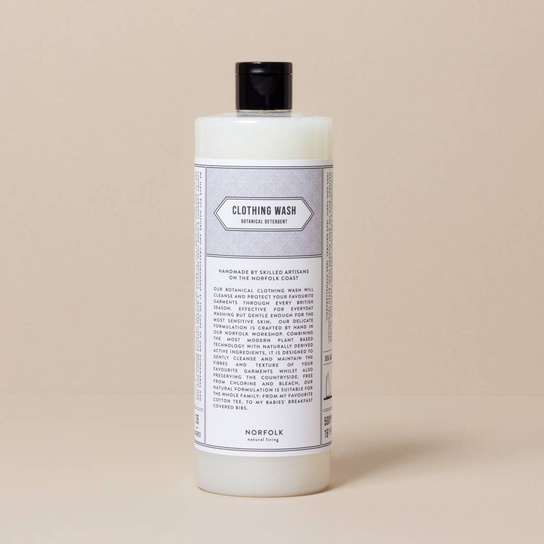 A white bottle of Norfolk Natural Living Coastal laundry detergent sits against a tan background. The label, in elegant typography, includes detailed text about the product.