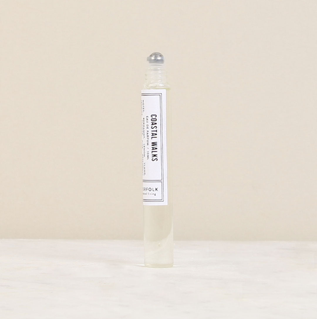 A clear rollerball perfume bottle labeled "Parfum de l'eau Coastal Walks" by Norfolk Natural Living, designed for unisex appeal, standing upright against a neutral beige background.