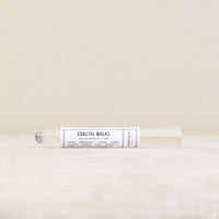 A clear rollerball perfume bottle labeled "Parfum de l'eau Coastal Walks" by Norfolk Natural Living on a beige background. The label has descriptions like "sea salt, dune grass, driftwood," "floral notes," and