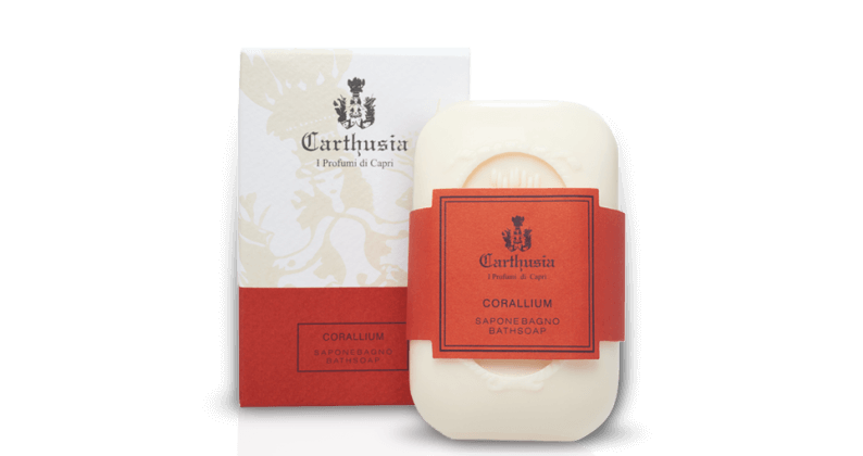 A bar of Carthusia I Profumi de Capri brand Corallium soap alongside its red and beige packaging, featuring elegant text and a coat of arms.
