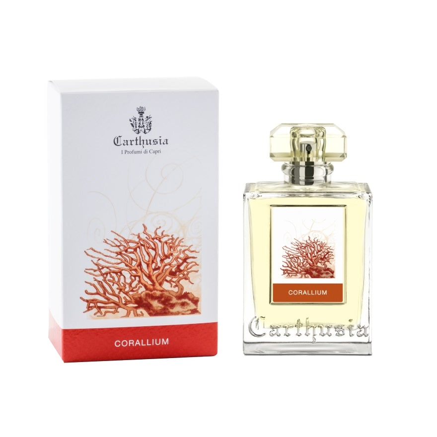 A bottle of Carthusia Corallium Eau de Parfum by Carthusia I Profumi de Capri next to its packaging. The clear glass bottle with a golden cap displays a red coral design, matching the elegant white and red box.