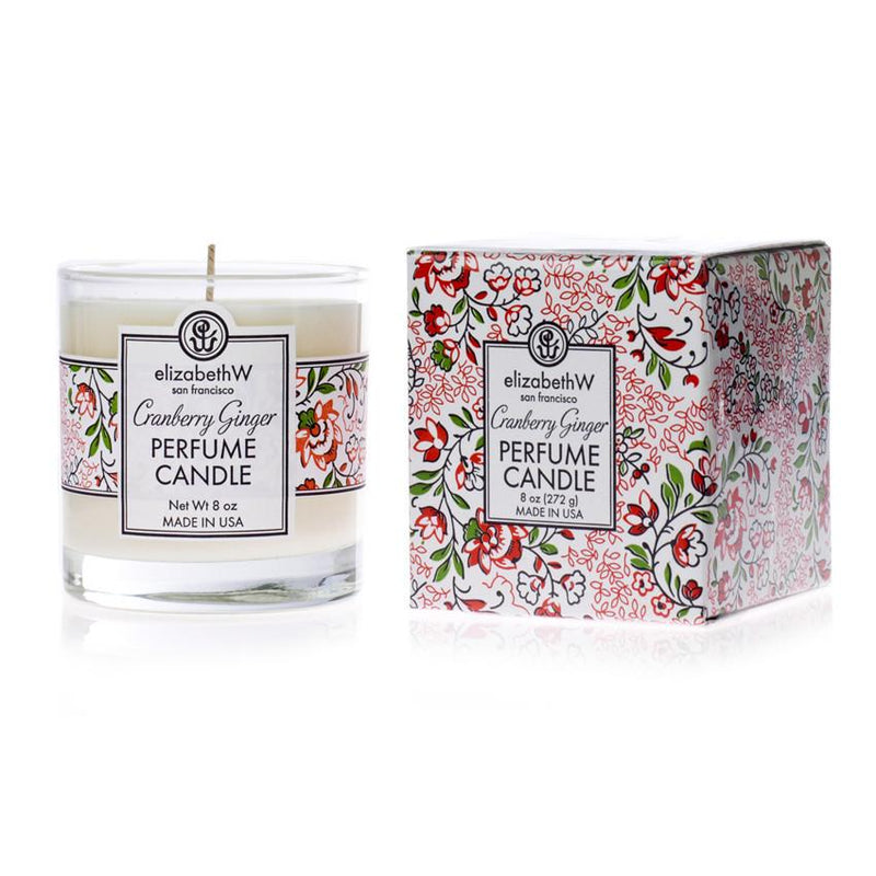 A elizabeth W Cranberry Ginger Candle in a clear glass holder next to its decorative box with a floral pattern in red, white, and green.