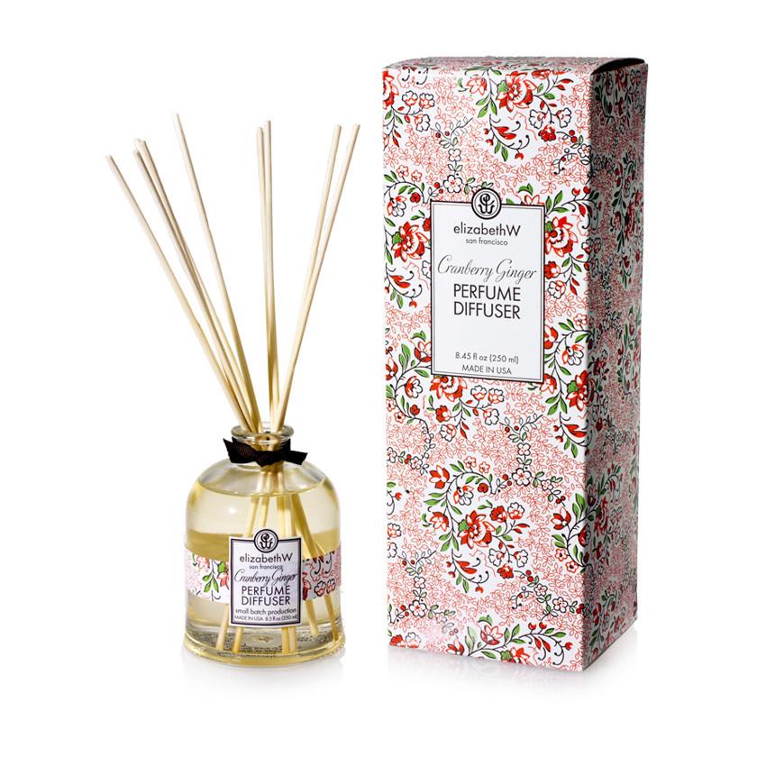 A glass perfume diffuser bottle with reed sticks, labeled "elizabeth W Cranberry Ginger Diffuser," next to its floral-patterned box, on a white background.