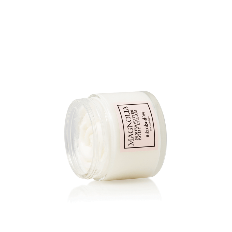 An open jar of elizabeth W Signature Magnolia Body Cream on a white background, showing its creamy texture inside.