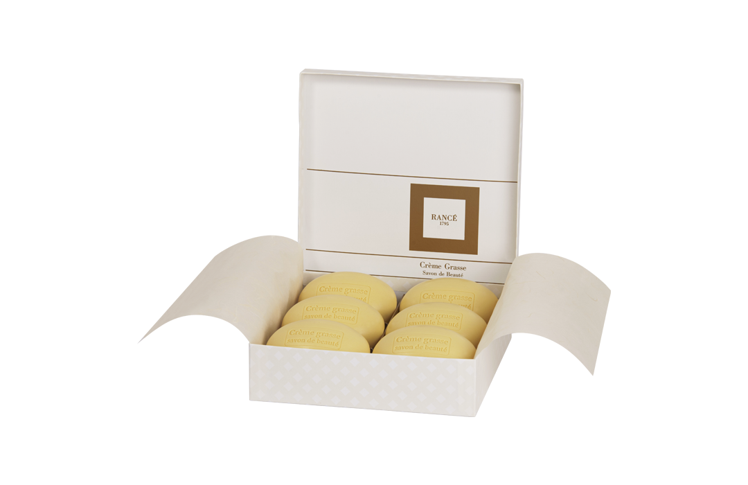 Open gift box displaying six round, yellow soaps of Rancé Classic Soap - Jasmine Créme Grasse, nestled in an elegant white holder with a gold-trimmed band around the inner box.