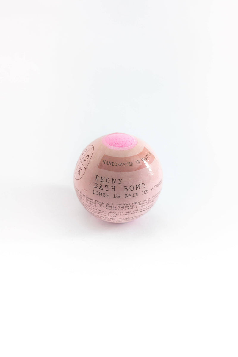 A pink SOAK Bath Co. - Peony-scented bath bomb with visible labels reading "Mother's Day bath bomb" and "handcrafted in xs" on a plain white background.