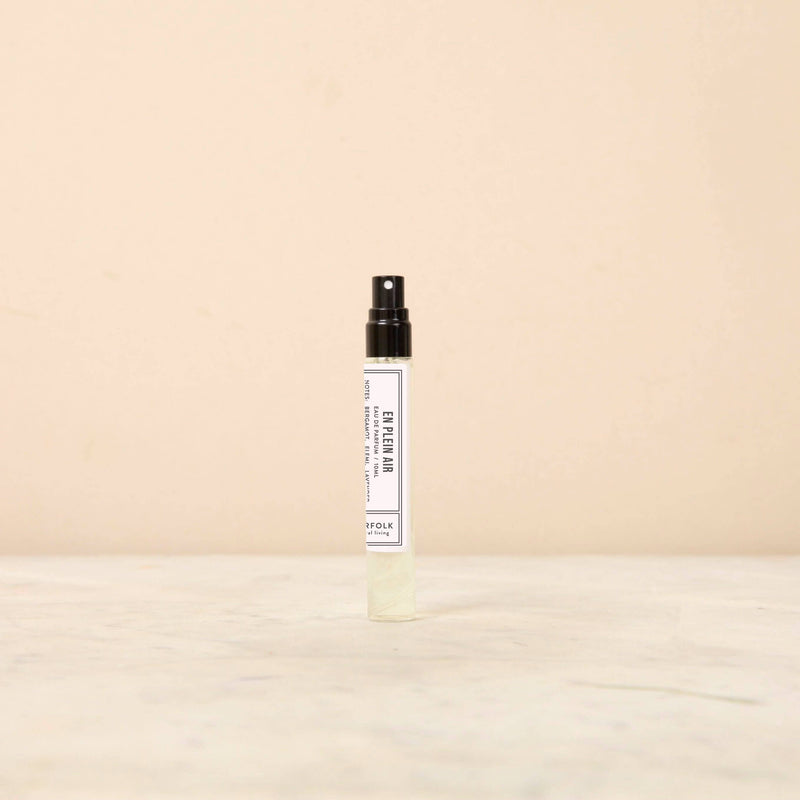A small, white, spray bottle labeled "Norfolk Natural Living En Plein Air Parfum 10ml" on a plain, beige background from Norfolk Perfumery.