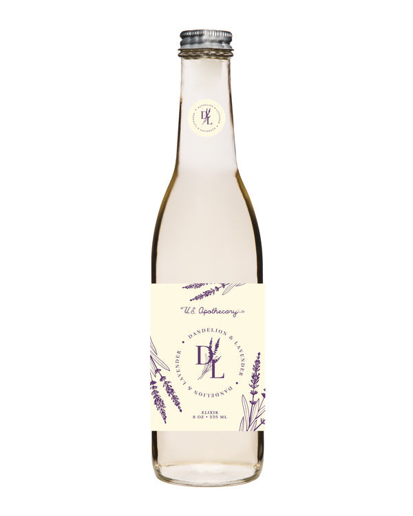 A clear glass bottle labeled "U.S. Apothecary Dandelion & Lavender Bath Elixir" filled with a pale amber liquid, featuring elegant purple floral artwork on the label, enhanced with natural plant extracts.
