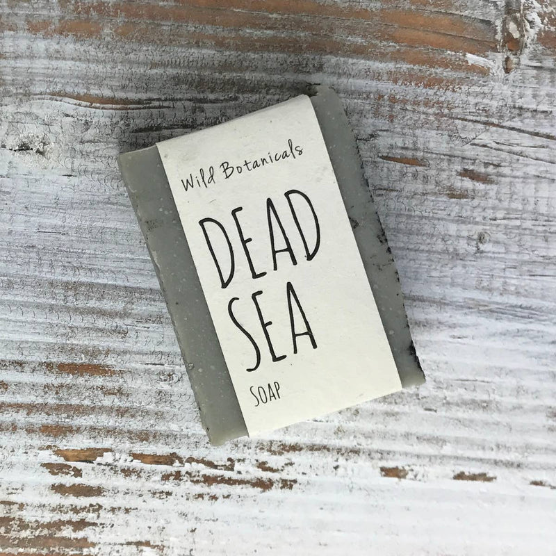 A bar of "Wild Botanicals Dead Sea Soap" from wild botanicals resting on a weathered wooden surface. The packaging is simple with handwritten-style lettering.