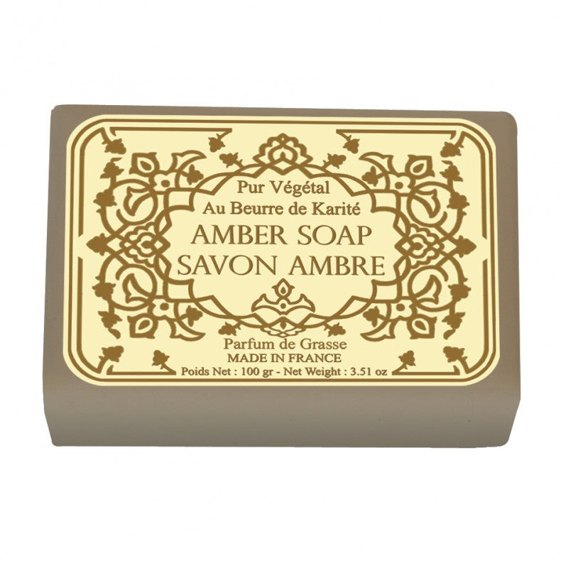 A bar of Le Blanc Amber Wrapped Soap with ornate gold and white labeling that includes details like "au beurre de karité," "made in France," and the product's weight, set against a plain background.