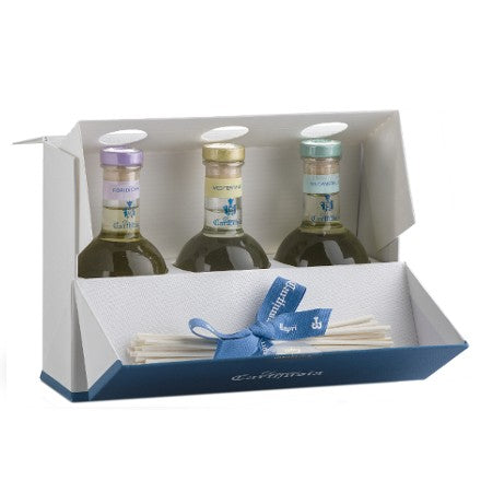 A Carthusia Home Diffuser Set containing three bottles of Carthusia perfumes with labels in shades of purple, green, and blue, packaged in a white and blue box with a bow and including dipping sticks.