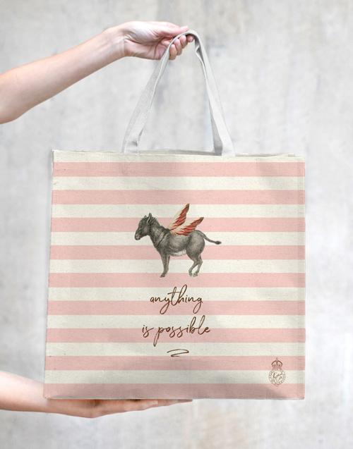 A person holds a Margot Elena TokyoMilk Tote Bag - Donkey Anything is Possible Market Tote featuring a whimsical illustration of a winged horse and the inspirational quote, "anything is possible," printed in cursive.