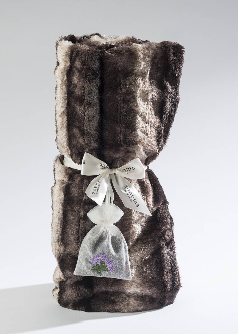 A luxurious Sonoma Timber Lake Cuddle Throw - Timber Lake Chinchilla wine bag wrapped with an elegant white ribbon labeled "season's greetings," accompanied by a delicate sachet of dried lavender tied to the ribbon.