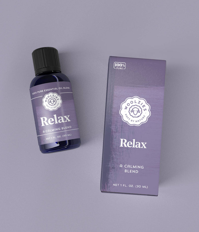 A bottle of "Woolzies Relax Essential Oil" next to its packaging box, both featuring purple labels with white text. The box and bottle are set on a light grey background.