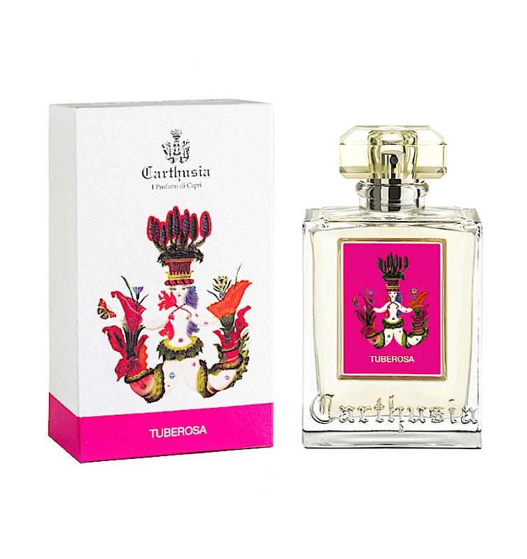 Image of a Carthusia I Profumi de Capri Tuberosa Eau de Parfum bottle next to its packaging. The bottle has a clear glass design with a gold cap and a label featuring a brightly colored, abstract art image. The matching box is white with pink.