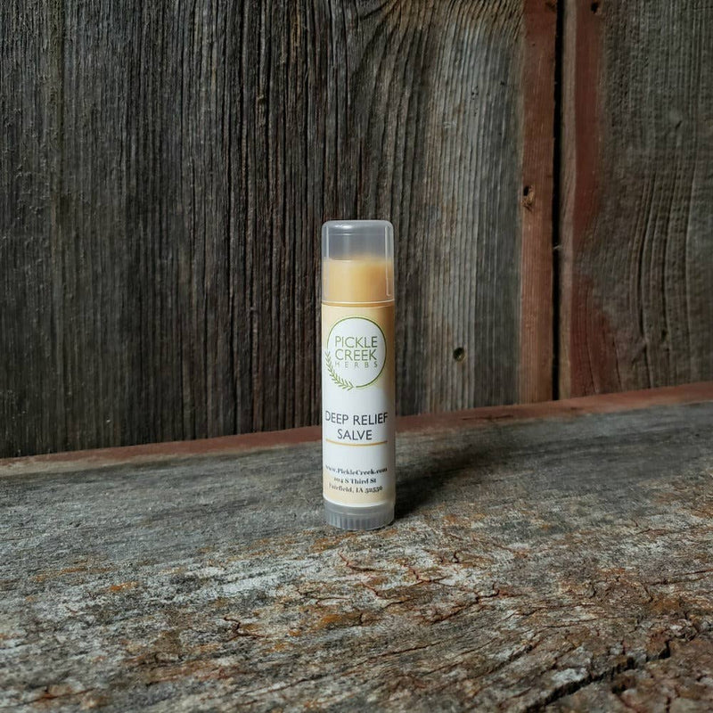 A tube of "Pickle Creek Herbs Deep Relief Salve" from Pickle Creek Herbs, standing on a wooden surface against a worn wooden backdrop.