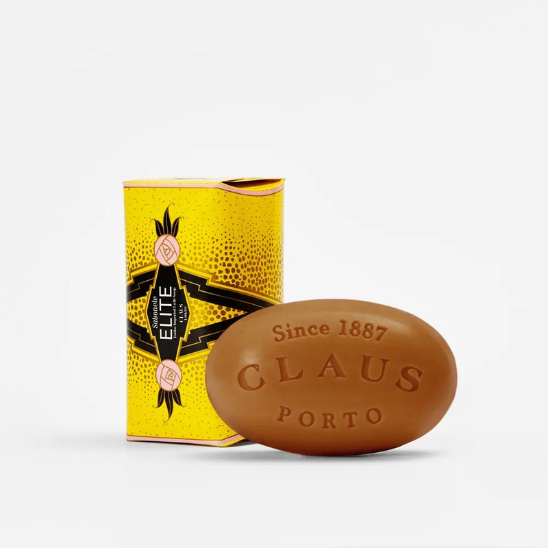 A Claus Porto Elite Tonka Imperial soap bar next to its vibrant yellow and black packaging, featuring intricate designs and the text "since 1887" on both the soap and the box.