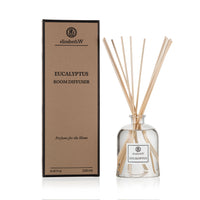 A glass bottle of environmentally friendly Elizabeth W Purely Essential Eucalyptus Diffuser with reeds next to its cardboard packaging labeled “elizabeth W eucalyptus room diffuser, perfume for the home.