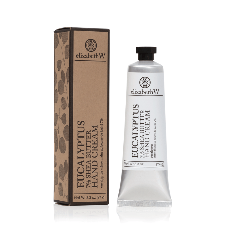 A tube of elizabeth W Purely Essential Eucalyptus Hand Cream beside its brown packaging box, both featuring an elegant eucalyptus leaf design. The tube is silver with a black cap.