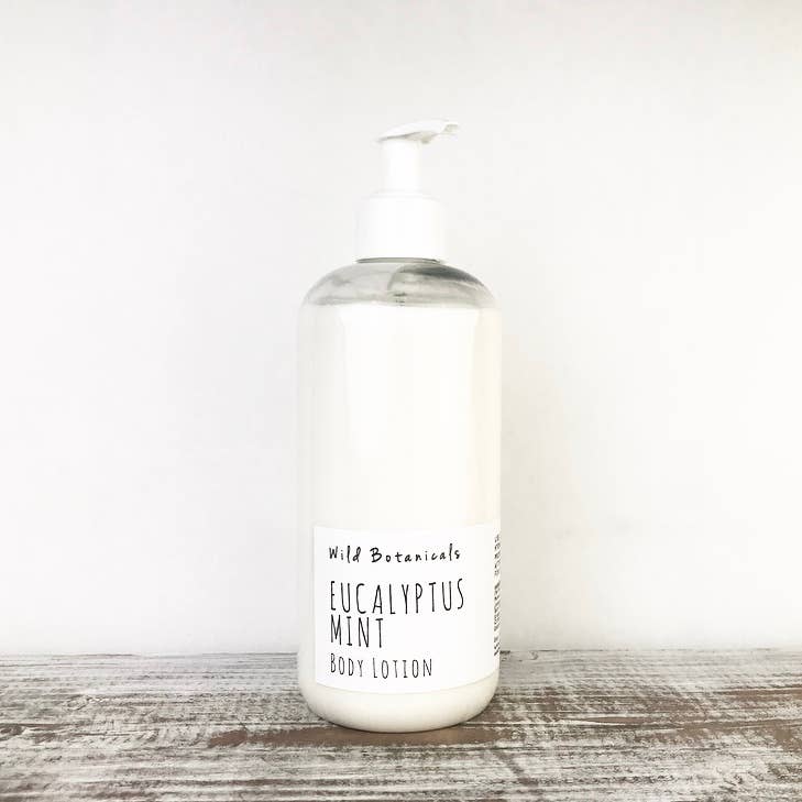 A clear bottle of Wild Botanicals Eucalyptus Mint Lotion with avocado oil and a pump dispenser, set against a plain white wooden background.